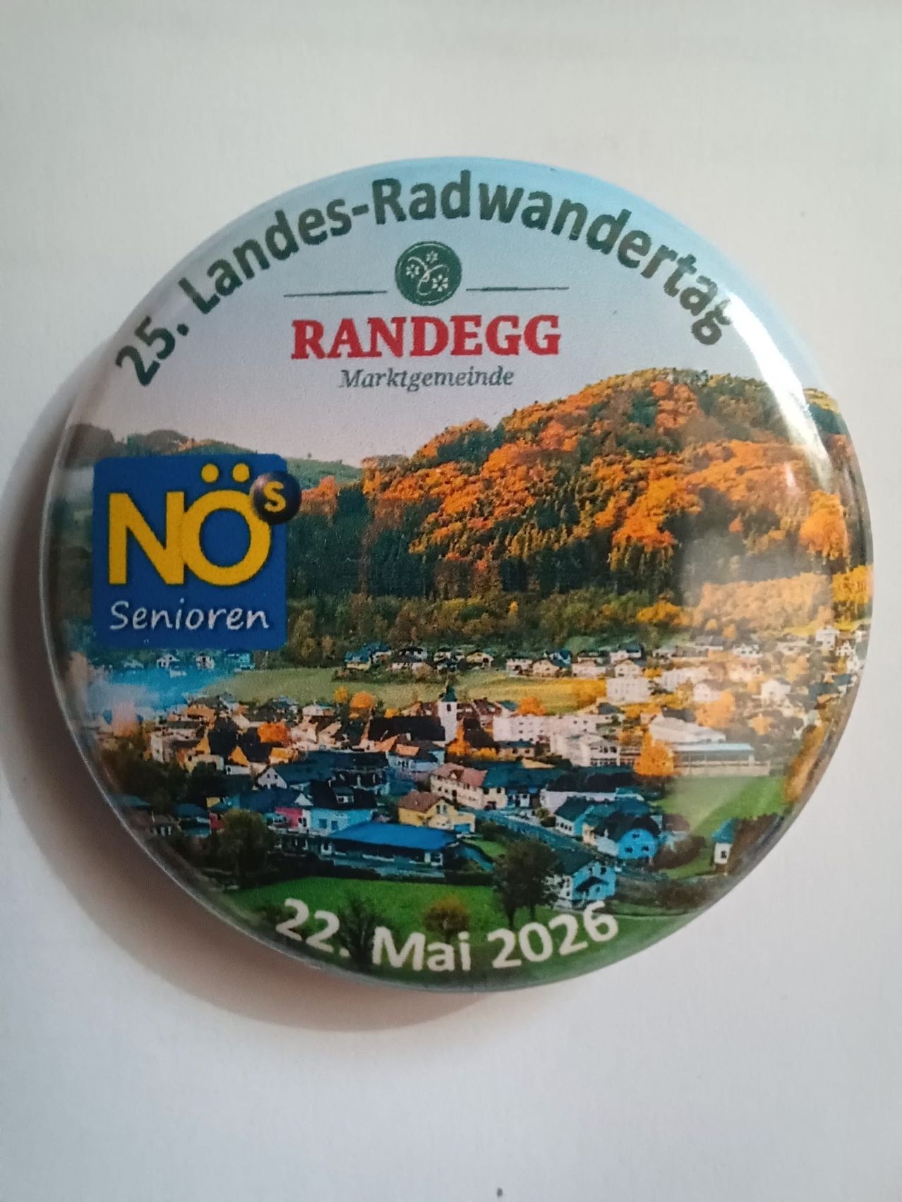 Ein rundes Abzeichen mit einer Dorfszene, '25. Landes-Radwanderungtag' und dem Datum 22. Mai 2026. Das Dorf ist von Hügeln und Bäumen umgeben. Das Abzeichen enthält auch den Namen Randegg und das Wort 'Senioren'.