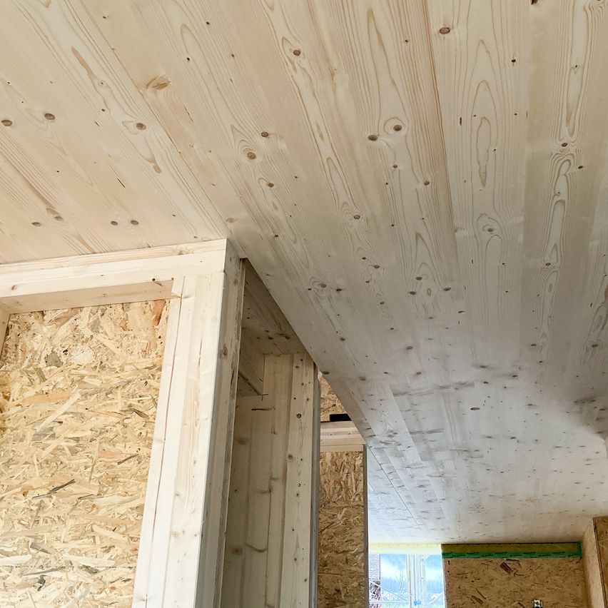 Close-up of a wooden ceiling and walls in a room under construction. The ceiling is made of pine wood with visible knots. Wooden panels form the walls.