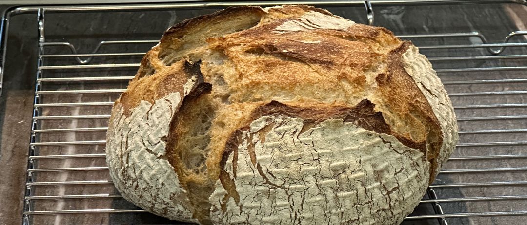 Ein frisch gebackenes Brot mit goldbrauner Kruste und rustikalem Aussehen, das auf einem Kühlgitter ruht.