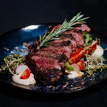 Ein Steak mit Rosmarin liegt auf einem Teller mit gemischten Gemüse und cremiger Sauce.