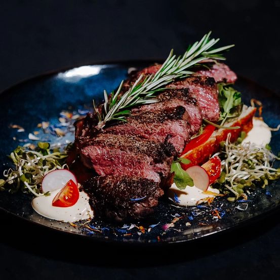 Ein Steak mit Rosmarin liegt auf einem Teller mit gemischten Gemüse und cremiger Sauce.