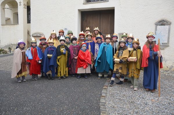 Eine Gruppe von Kindern in Kostümen, einige mit Kronen, posiert für ein Foto vor einem Gebäude.