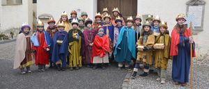 Eine Gruppe von Kindern in Kostümen, einige mit Kronen, posiert für ein Foto vor einem Gebäude.