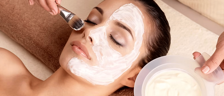 Eine Frau liegt auf einem Handtuch und bekommt eine Gesichtsbehandlung mit Pinsel und Creme.