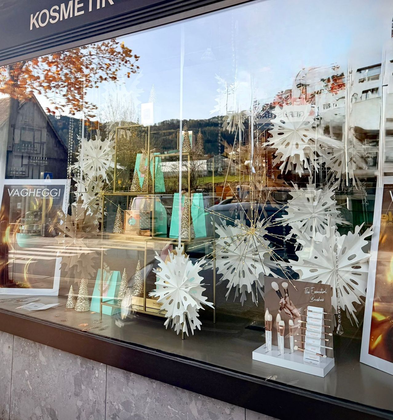 A shop window with a festive display of white snowflakes, a golden stand, and a sign that reads 'Vagheggi'. The display includes various decorative items and products.