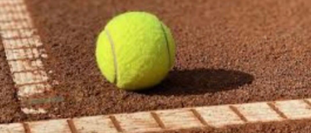 Ein Tennisball liegt auf einem braunen Sandtennisplatz. Er befindet sich in der Nähe der weißen Begrenzungslinie des Platzes.