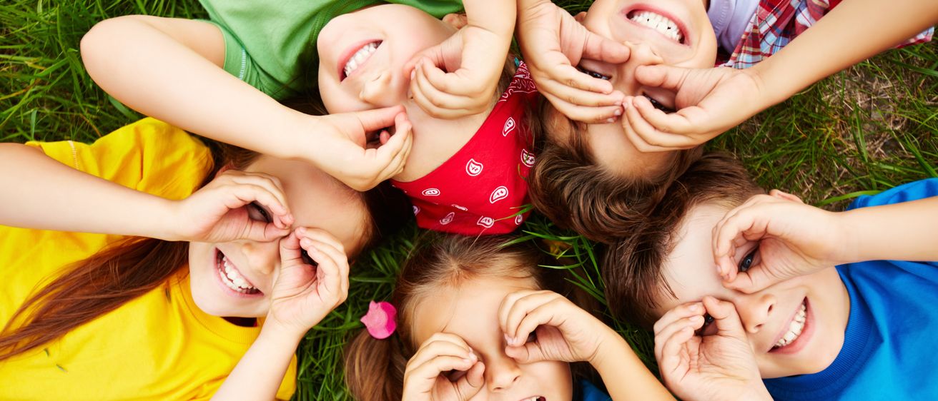 Eine Gruppe von Kindern liegt auf dem Gras und macht lustige Gesichter mit ihren Händen.