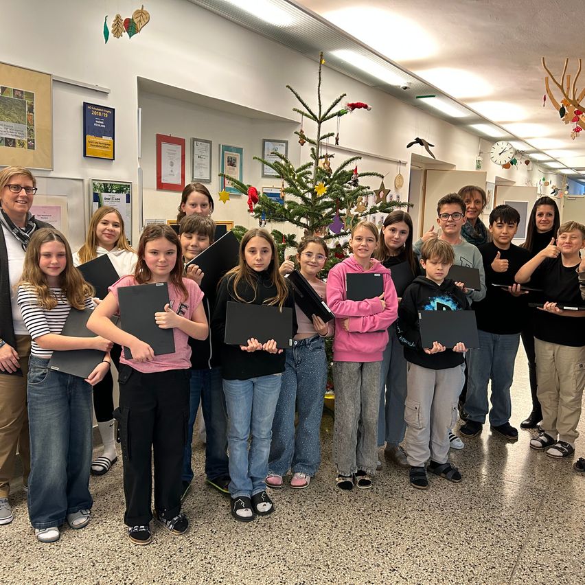 Eine Gruppe von Schülern und Lehrern posiert für ein Foto in einem Flur mit einem geschmückten Weihnachtsbaum und Ankündigungstafeln im Hintergrund.