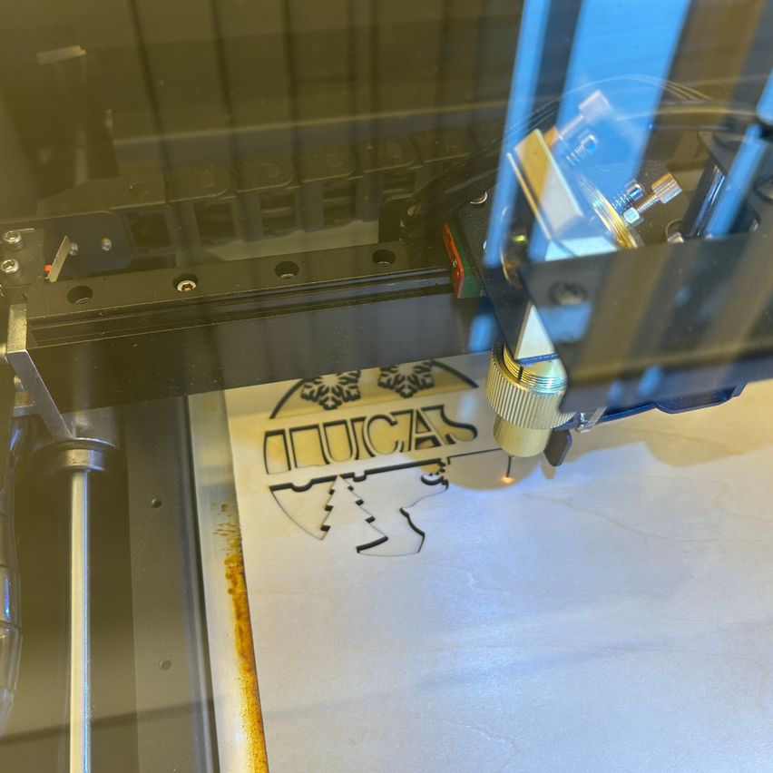 Eine Nahaufnahme einer Maschine mit einer goldenen Spitze, die ein Baumdesign auf einem weißen Blatt schneidet. Die Maschine ist von Glas umschlossen.