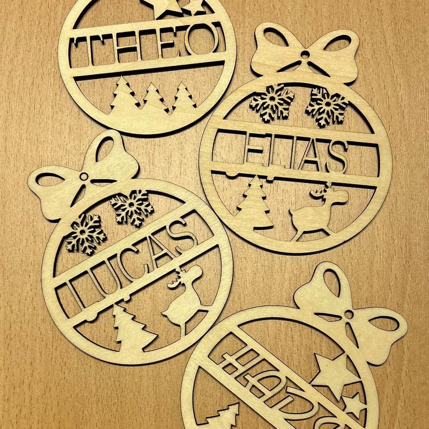 Fünf Holzornamente sind auf einer braunen Oberfläche zu sehen. Jedes Ornament hat ein einzigartiges Design mit verschiedenen Namen und weihnachtlichen Illustrationen. Die Ornamente sind kreisförmig mit einer Schleife an der Seite.