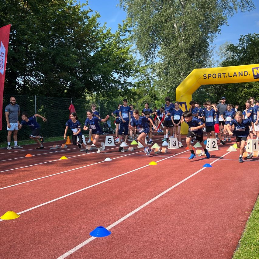 Eine Gruppe junger Athleten bereitet sich auf den Start eines Rennens in Sport.Land vor, mit Nummern auf ihren Trikots und Kegel, die die Bahnen markieren.