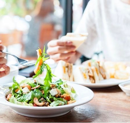 Zwei Personen essen in einem Restaurant. Eine hält einen Salat mit einer Gabel.