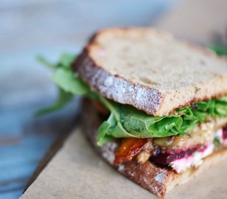 Ein Sandwich mit einer Mischung aus Grünzeug, Rote Bete und anderen Zutaten, auf einem braunen Papierservietten auf einem blauen Tisch platziert.