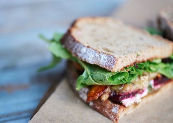 Ein Sandwich mit einer Mischung aus Grünzeug, Rote Bete und anderen Zutaten, auf einem braunen Papierservietten auf einem blauen Tisch platziert.