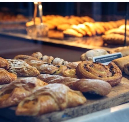 Ein Holzschneidebrett zeigt eine Auswahl an Gebäck, darunter Croissants und Brötchen, unter warmer Beleuchtung.