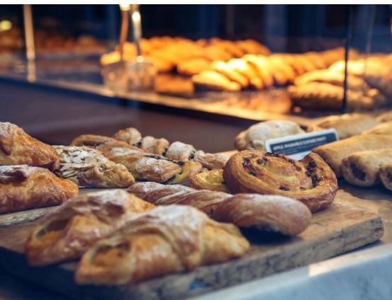 Ein Holzschneidebrett zeigt eine Auswahl an Gebäck, darunter Croissants und Brötchen, unter warmer Beleuchtung.