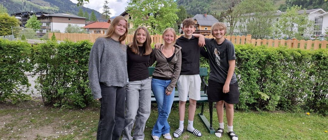 Fünf Personen stehen in einem Garten mit Bergen im Hintergrund. Sie posieren für ein Foto in einem sonnigen Außenbereich.