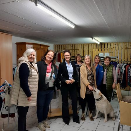 Eine Gruppe von Frauen und ein Hund stehen in einem Raum mit Holzwänden, lächeln und posieren für ein Foto.