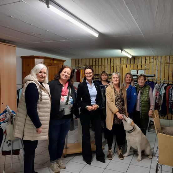 Eine Gruppe von Frauen und ein Hund stehen in einem Raum mit Holzwänden, lächeln und posieren für ein Foto.