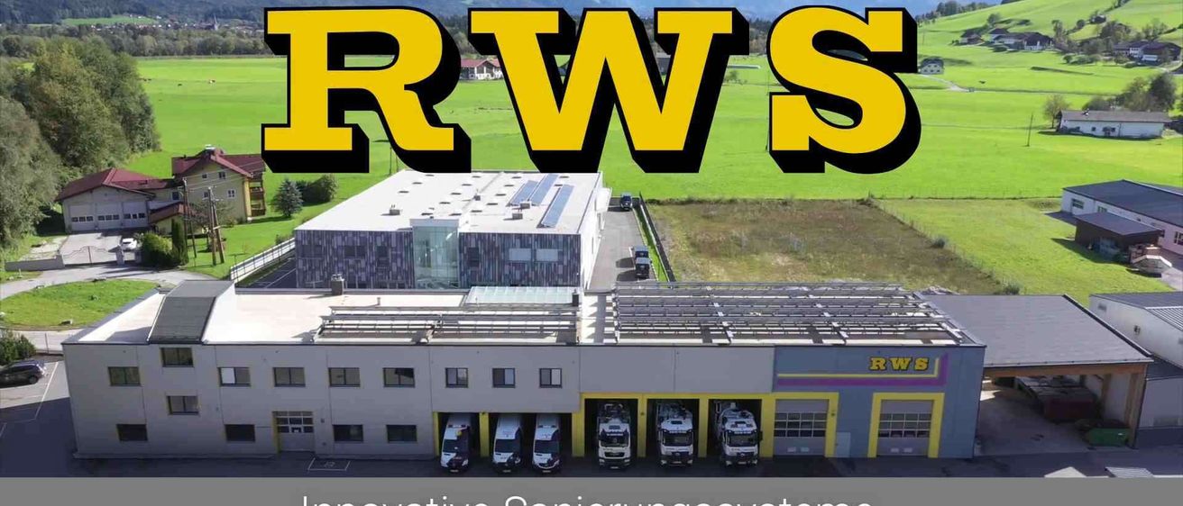 Eine Luftaufnahme einer Einrichtung mit mehreren geparkten Fahrzeugen, beschriftet mit 'RWS' in gelbem Text. Es hat Solarmodule auf dem Dach, und der Text darunter lautet 'Innovative Sanierungsysteme Wartung - Reinigung - Entsorgung.' Berge sind im Hintergrund sichtbar.