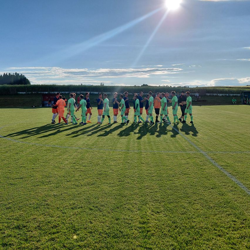 Eine Fußballmannschaft in grünen Trikots versammelt sich auf einem sonnigen Feld, wobei Spieler und Trainer in einer Reihe stehen.