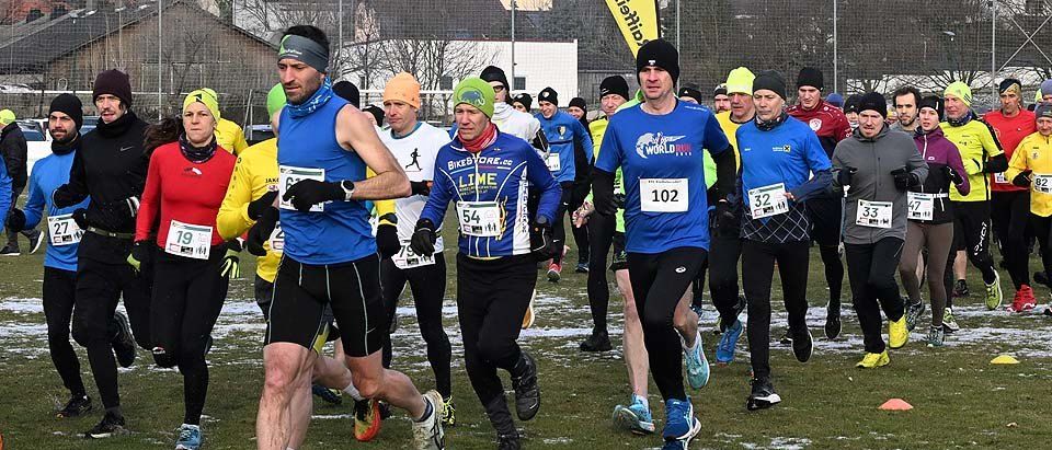 Marathonteilnehmer mit nummerierten Startnummern auf einem Rasenfeld, teilweise mit Mützen und Handschuhen.