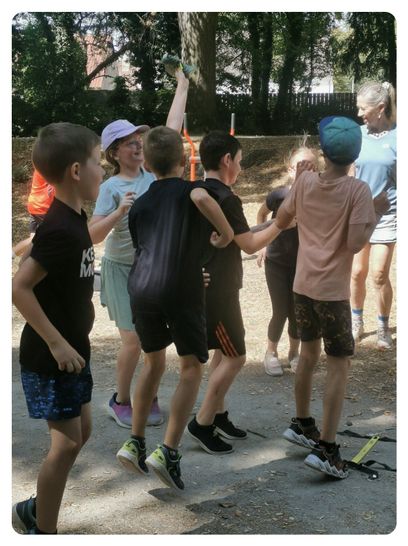Eine Gruppe von Kindern und Erwachsenen spielt ein Spiel in einem Park, wobei eine Frau ihren Arm erhebt.