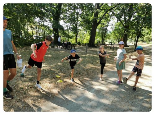 Eine Gruppe von Kindern spielt in einem Park mit gelben Markierungen auf dem Boden. Ein Kind läuft auf die Markierungen zu.