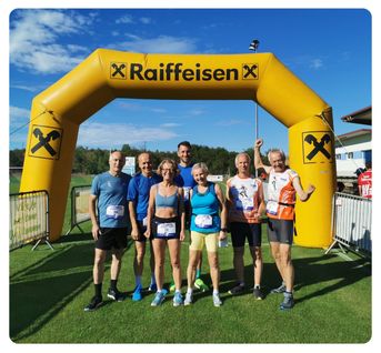 Eine Gruppe von sechs Läufern in Sportkleidung posiert für ein Foto unter einem gelben Raiffeisen-Bogen auf einem Rasenfeld.