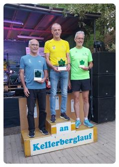 Drei Männer stehen auf einem Podest mit Trophäen und lächeln für ein Foto. Der Mann links trägt ein blaues Shirt, der in der Mitte ein gelbes Shirt und der rechts ein grünes Shirt. Hinter ihnen steht eine Bühne mit Musikinstrumenten und Lautsprechern.