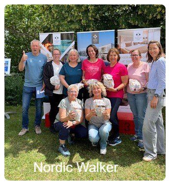 Eine Gruppe von Menschen posiert für ein Foto im Freien, lächelt und hält Tüten in der Hand. Ein Mann zeigt den Daumen nach oben. Das Foto ist mit Nordic Walker beschriftet.