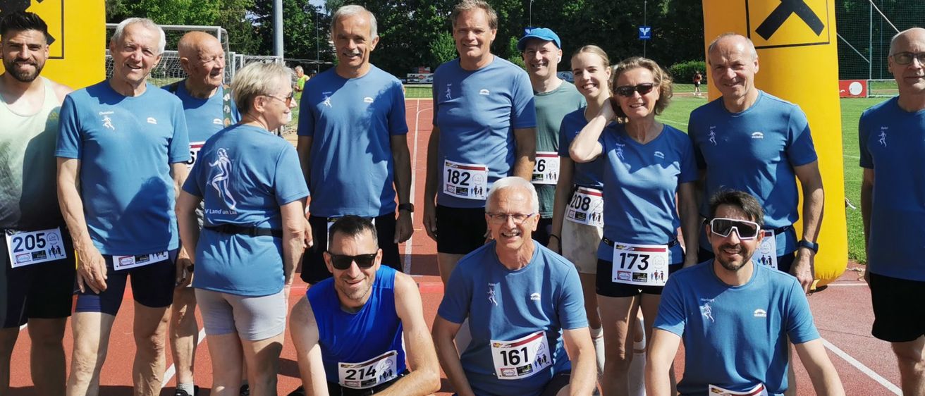 Eine Gruppe von Menschen in blauen Shirts und mit Sonnenbrillen posiert für ein Foto auf einer Laufbahn. Sie sind wahrscheinlich Teilnehmer eines von Raiffeisen gesponserten Marathons.