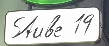 Ein grünes rundes Schild für Gosser Bier. Darunter steht ein weißes Schild mit 'Stube 19'.