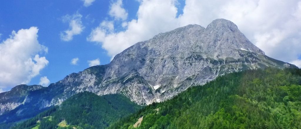 Eine Bergkette mit felsigem Gelände und grünen Bäumen unter einem blauen Himmel mit Wolken.