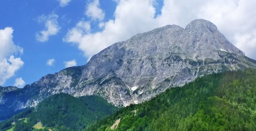 Eine Bergkette mit felsigem Gelände und grünen Bäumen unter einem blauen Himmel mit Wolken.