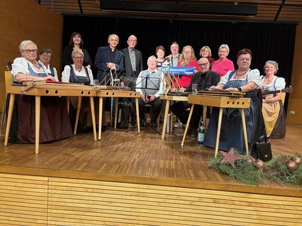 Eine Gruppe von Menschen in traditioneller Kleidung sitzt mit Musikinstrumenten und Dekorationen auf einer Bühne.