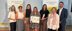 Eine Gruppe von Frauen und zwei Männer stehen vor einem Banner mit den Worten Land Kärnten. Die Frau in der Mitte hält ein Zertifikat.