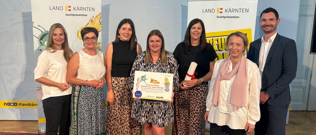 Eine Gruppe von Frauen und zwei Männer stehen vor einem Banner mit den Worten Land Kärnten. Die Frau in der Mitte hält ein Zertifikat.