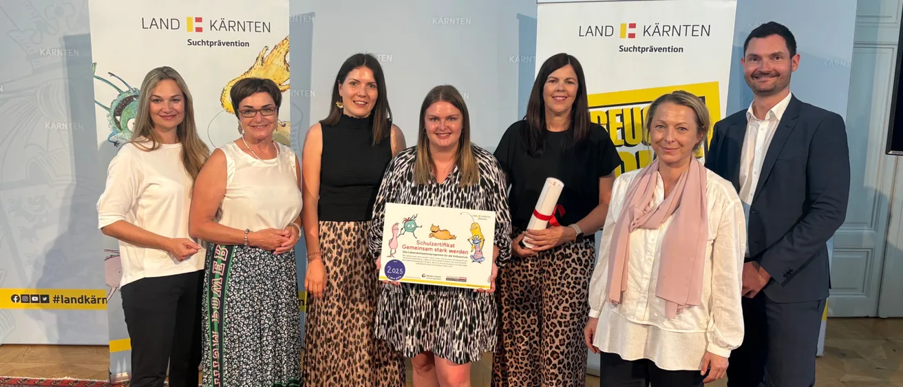Eine Gruppe von Frauen und zwei Männer stehen vor einem Banner mit den Worten Land Kärnten. Die Frau in der Mitte hält ein Zertifikat.