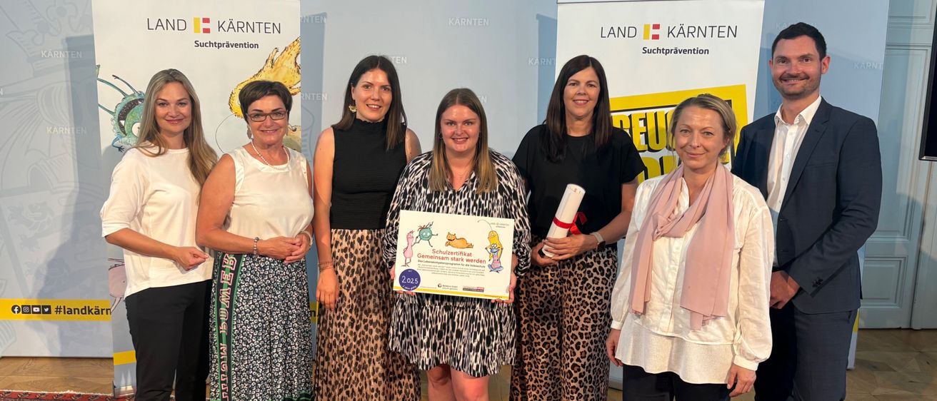 Eine Gruppe von Frauen und zwei Männer stehen vor einem Banner mit den Worten Land Kärnten. Die Frau in der Mitte hält ein Zertifikat.
