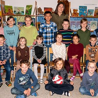 Eine Gruppe von Kindern und einer Frau posiert für ein Foto in einem Klassenzimmer mit Sonnenblumendekorationen.