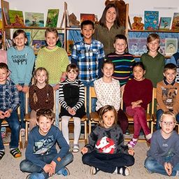 Eine Gruppe von Kindern und einer Frau posiert für ein Foto in einem Klassenzimmer mit Sonnenblumendekorationen.