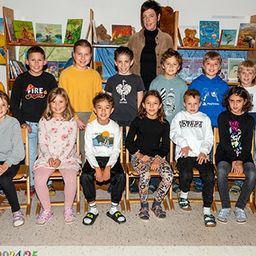 Ein Klassenfoto von jungen Schülern, einer Lehrerin und Sonnenblumen im Hintergrund.