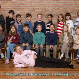 Eine Gruppe von Kindern und Erwachsenen posiert für ein Foto vor einer Ziegelwand. Der Text auf der Wand lautet 'Volksschule Kotschach - Mauthen 2023.'