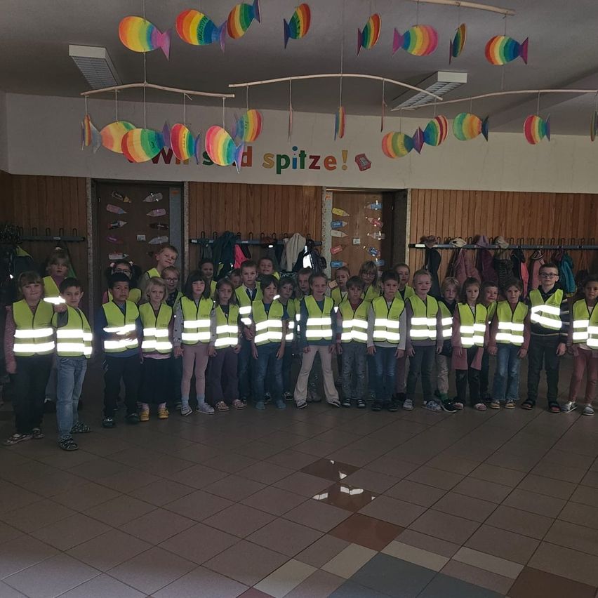 Eine Gruppe von Kindern in Warnwesten posiert für ein Foto in einem Raum mit Holzwand und Fischdekorationen.