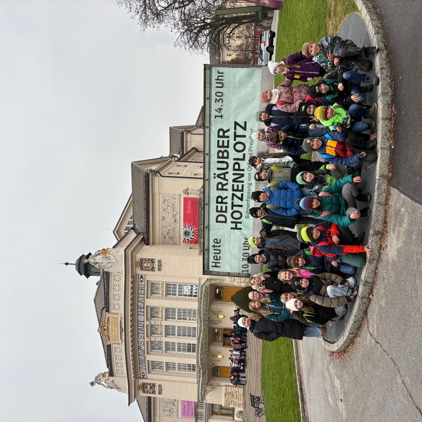 Eine Gruppe von Menschen posiert vor einem großen Banner vor einem historischen Gebäude. Das Banner trägt in fetten Buchstaben 'Der Räuber Hotzenplotz'.