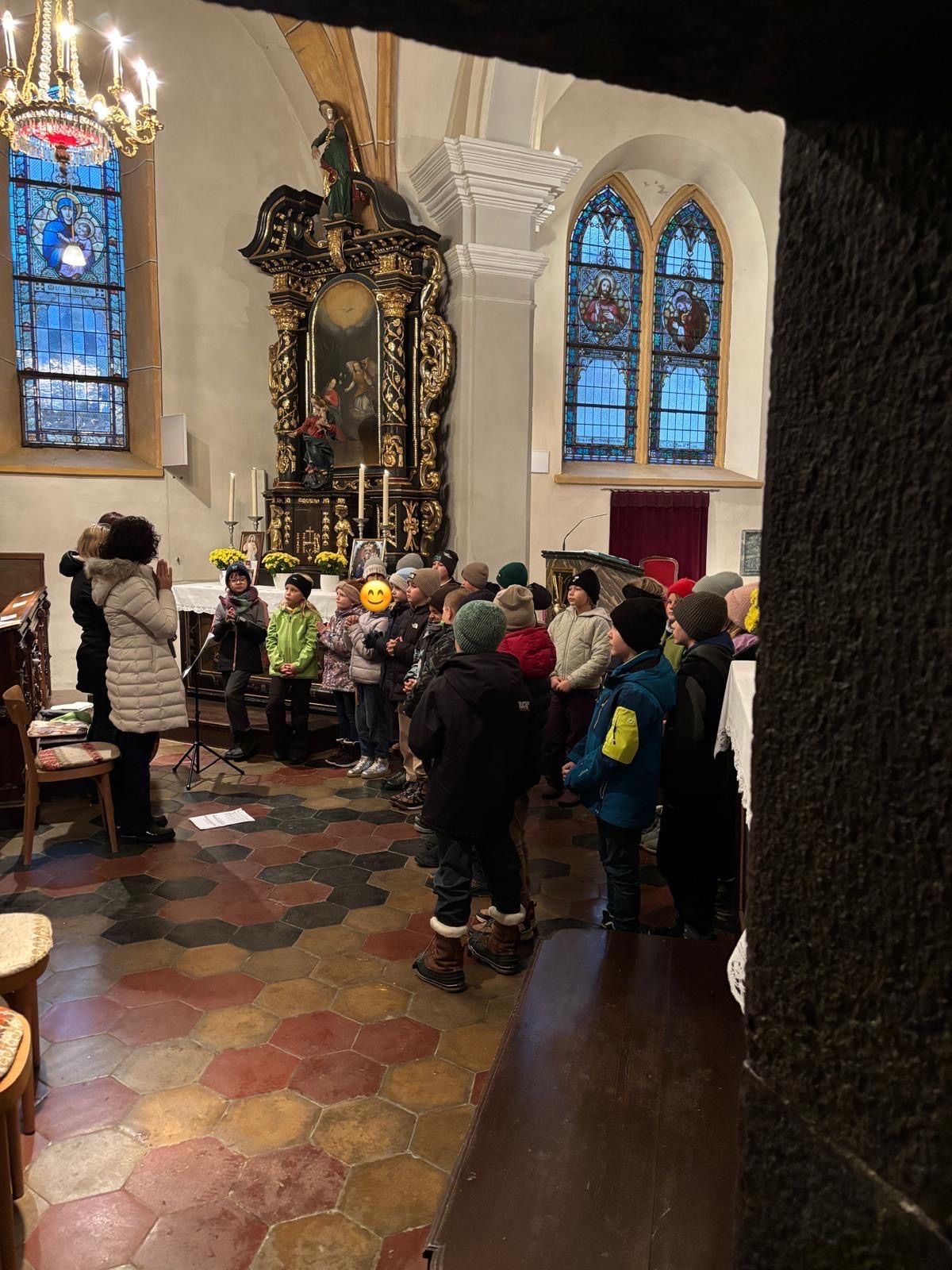 Eine Gruppe von Kindern und Erwachsenen versammelt sich in einer Kirche und steht vor einem Altar, der mit Blumen und Kerzen geschmückt ist.