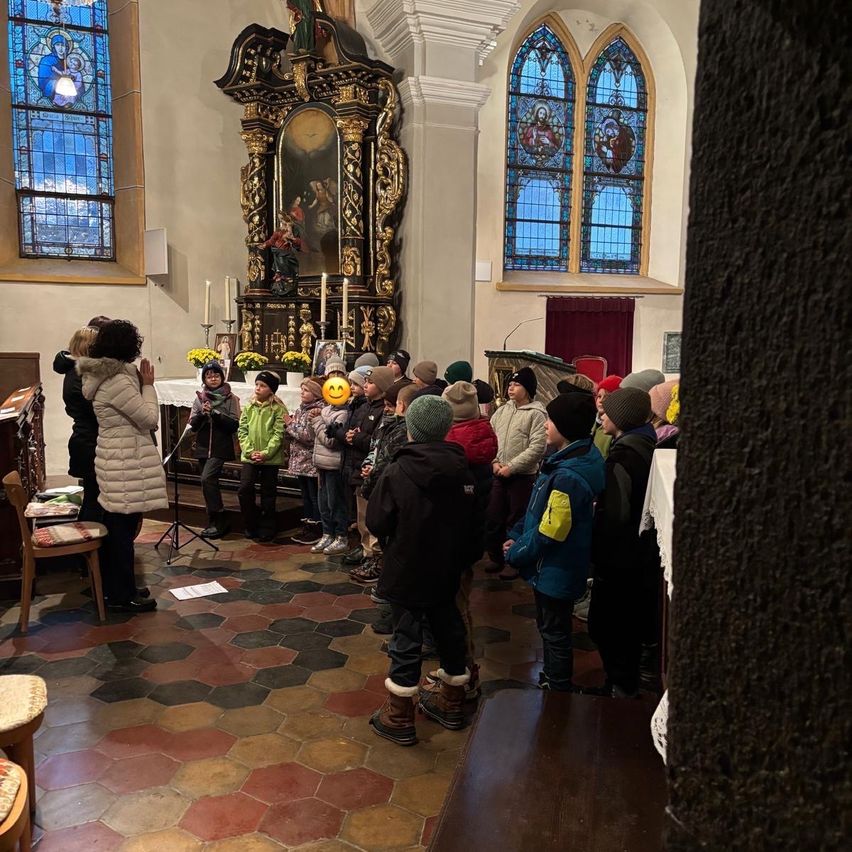 Eine Gruppe von Kindern und Erwachsenen versammelt sich in einer Kirche und steht vor einem Altar, der mit Blumen und Kerzen geschmückt ist.