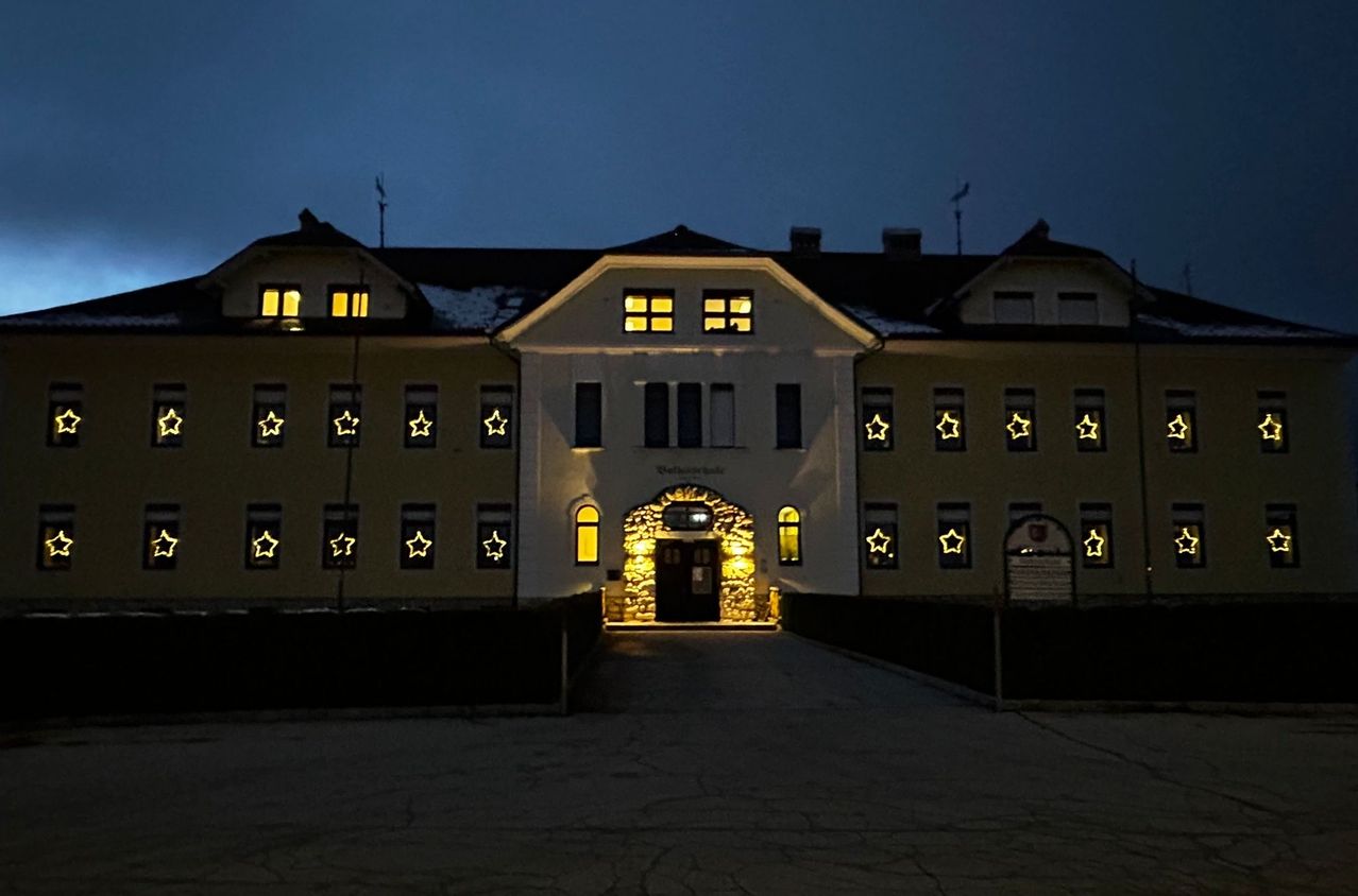 Ein Gebäude mit leuchtenden gelben Sternen bei Nacht. Der Eingang ist mit warmem gelbem Licht beleuchtet und mehrere Fenster sind erleuchtet.