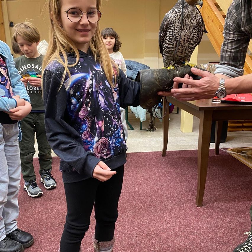 Ein junges Mädchen mit Brille hält einen Raubvogel an ihrer behandschuhten Hand, während andere zusehen.